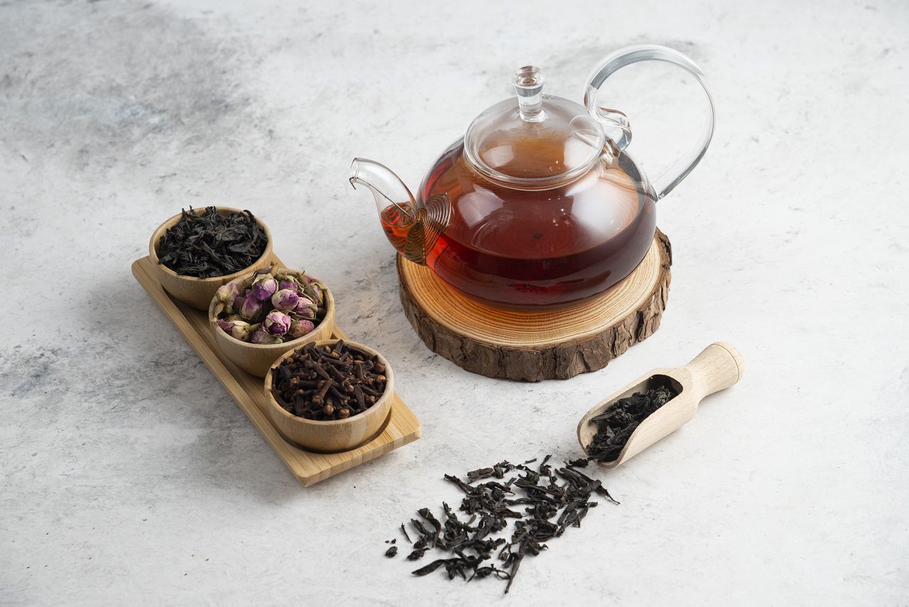 A glass teapot with wooden bowls of loose teas