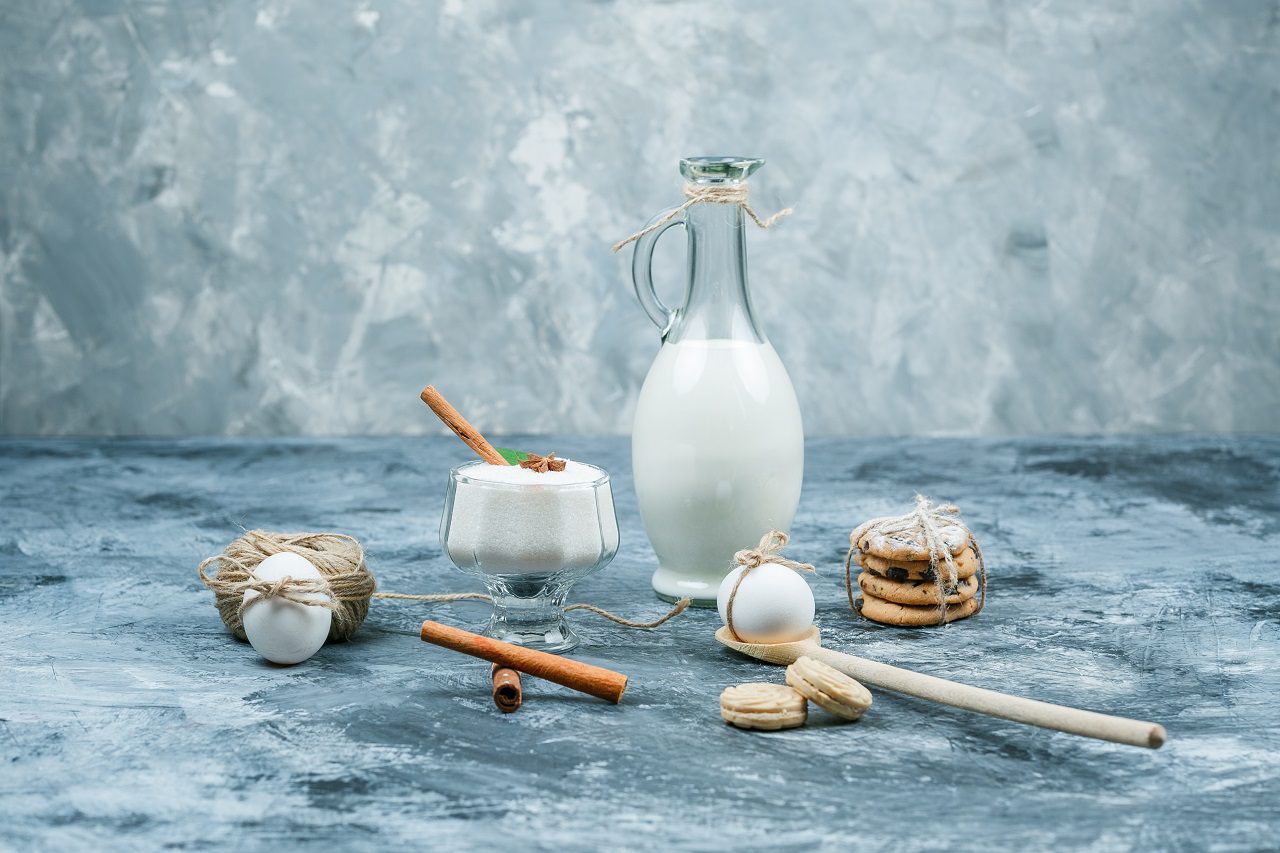 Close-up a jug of milk and a glass bowl of yogurt with cookies,eggs,clew and cinnamon on dark blue and grey marble background. horizontal