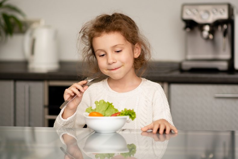 A cute girl eats a salad from fresh vegetables. Healthy food. Childhood.
