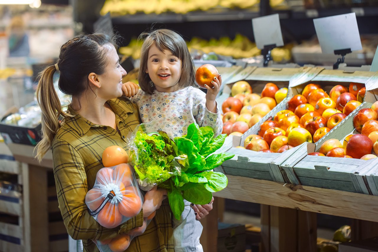 Family in the supermarket. Beautiful young mom and her little daughter smiling and buying food.
