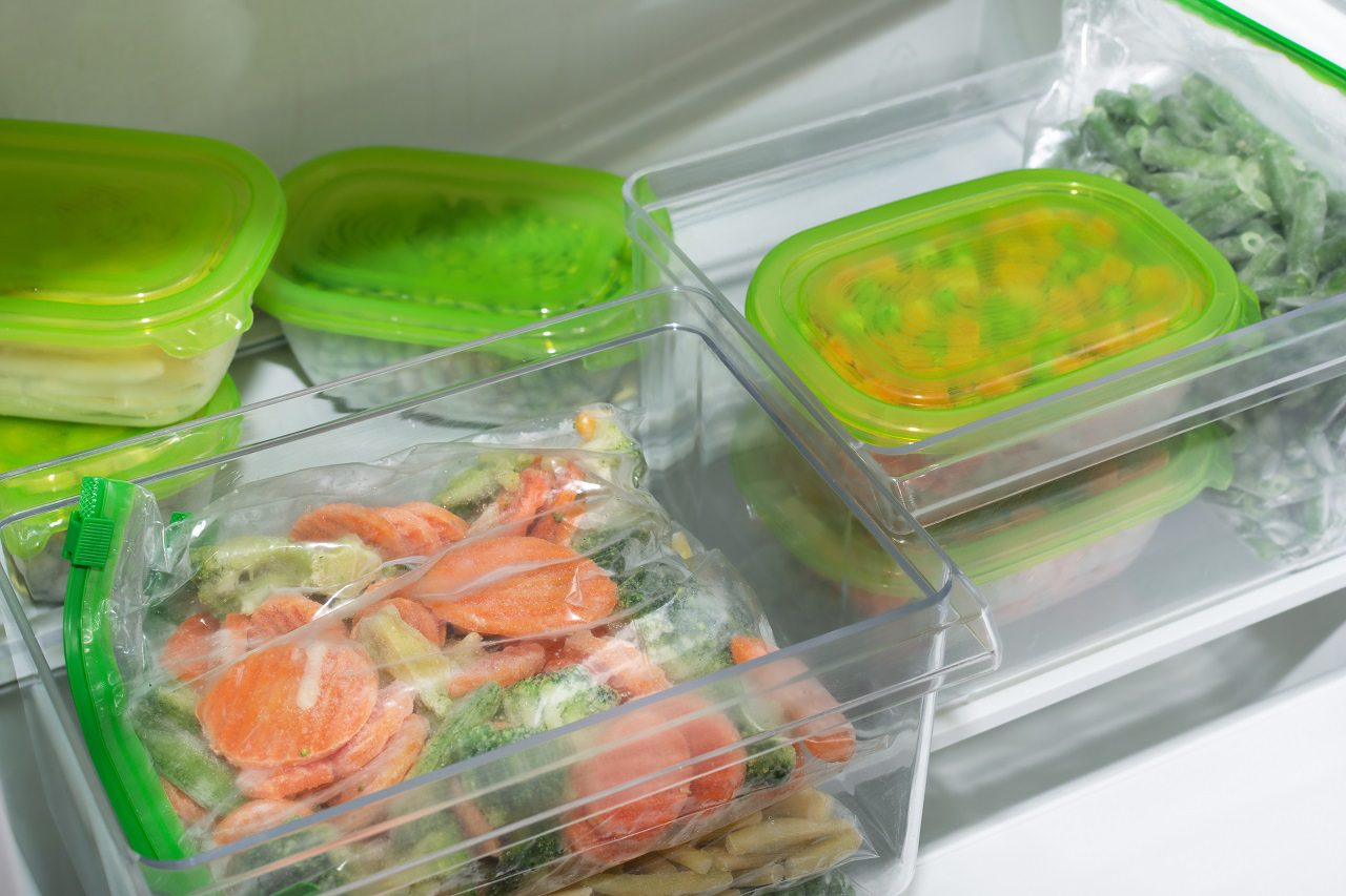 Plastic containers and bags with different frozen vegetables in