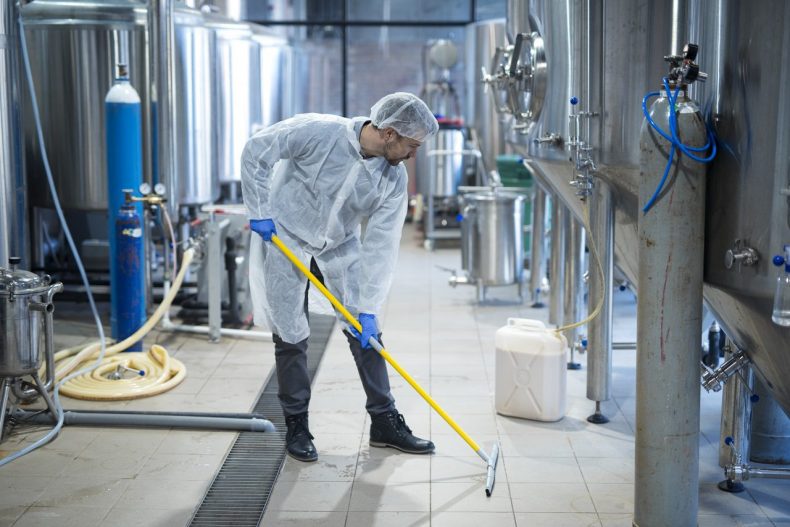 Professional industrial cleaner in protective uniform cleaning floor of food processing plant.