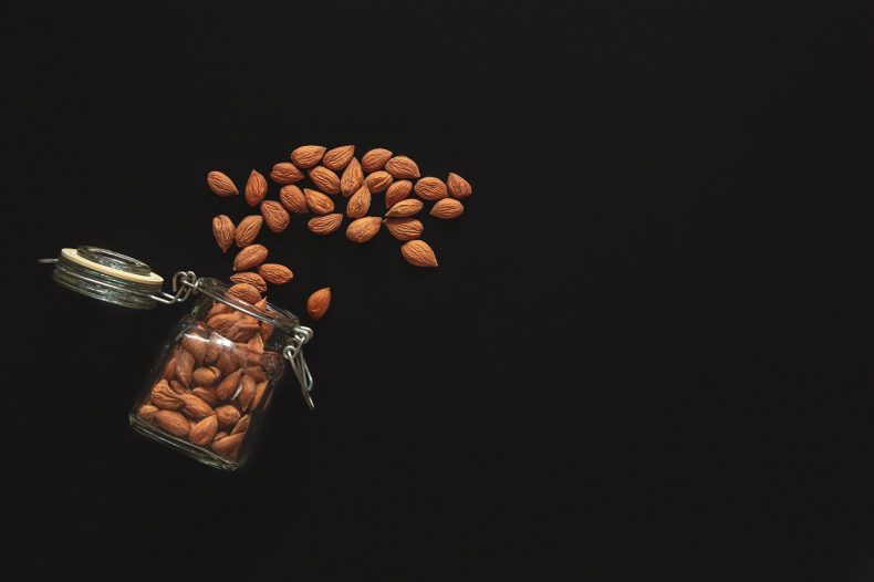 Scattered almond nuts on a black background, flat lay.