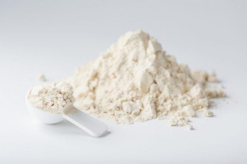 Whey protein isolate with a measuring spoon on a white background.