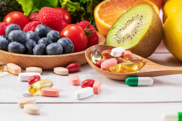 Selective focus shot of fresh fruits and vegetables with different medicine on a wooden spoon